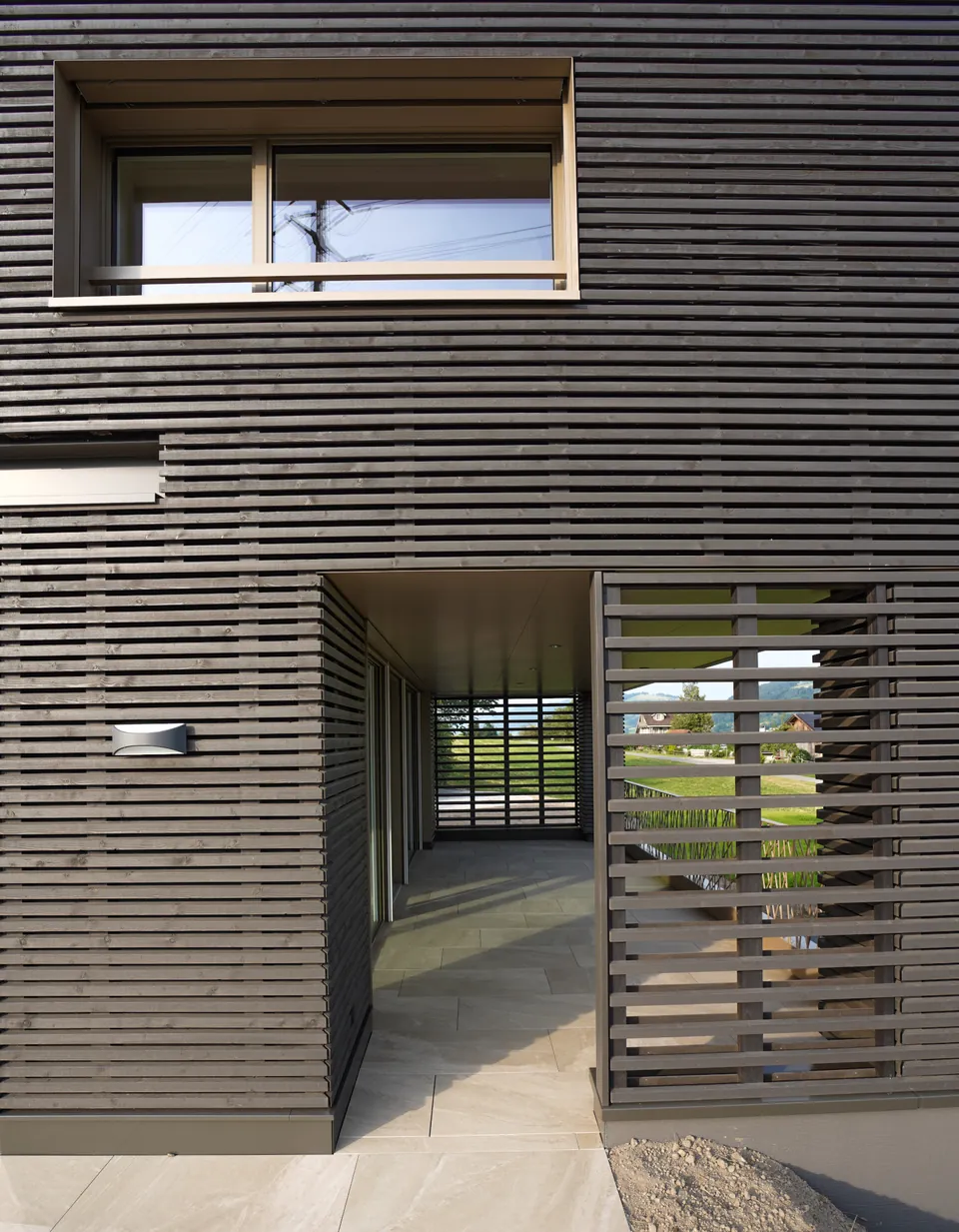 Dunkle Lattenfassade mit Fenster und Schiebeladen
