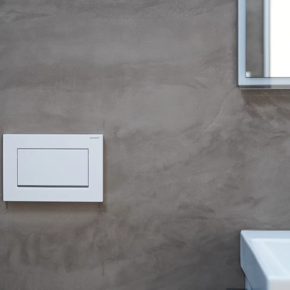Graubraune fugenlose Wand mit weisser WC-Drückerplatte