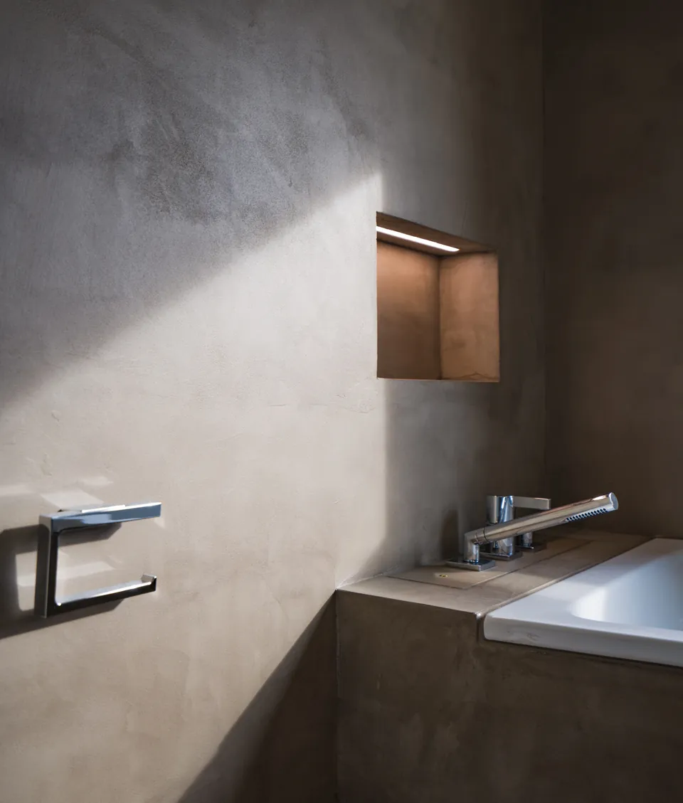 Fugenlose Wand in warmem Grau neben der Badewanne, mit Holznische