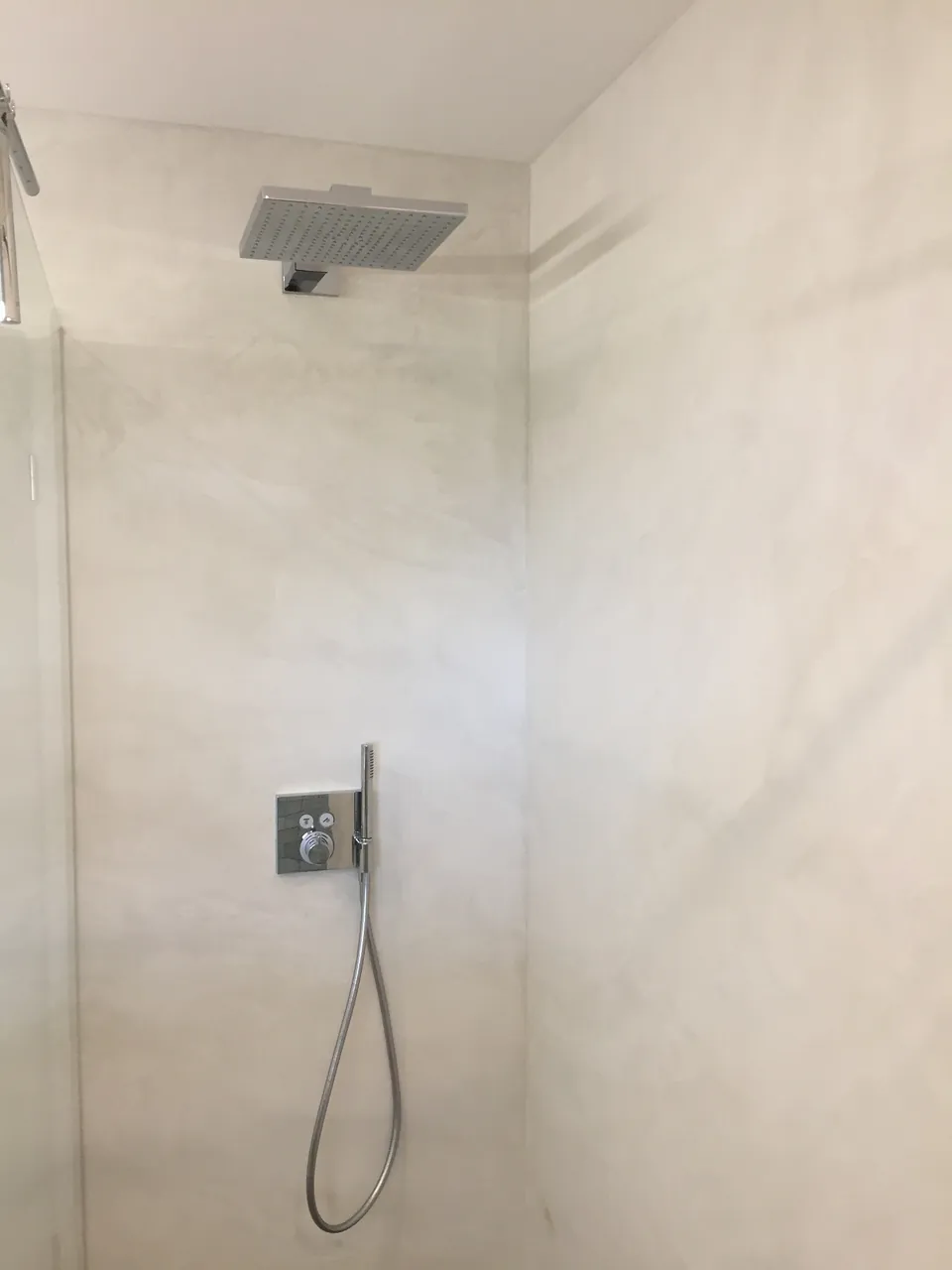 Dusche mit hellen, fugenlosen Wänden und Regenbrause