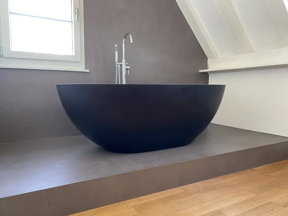 Freistehende dunkle Badewanne auf einem fugenlos belegten Podest unter der Dachschräge