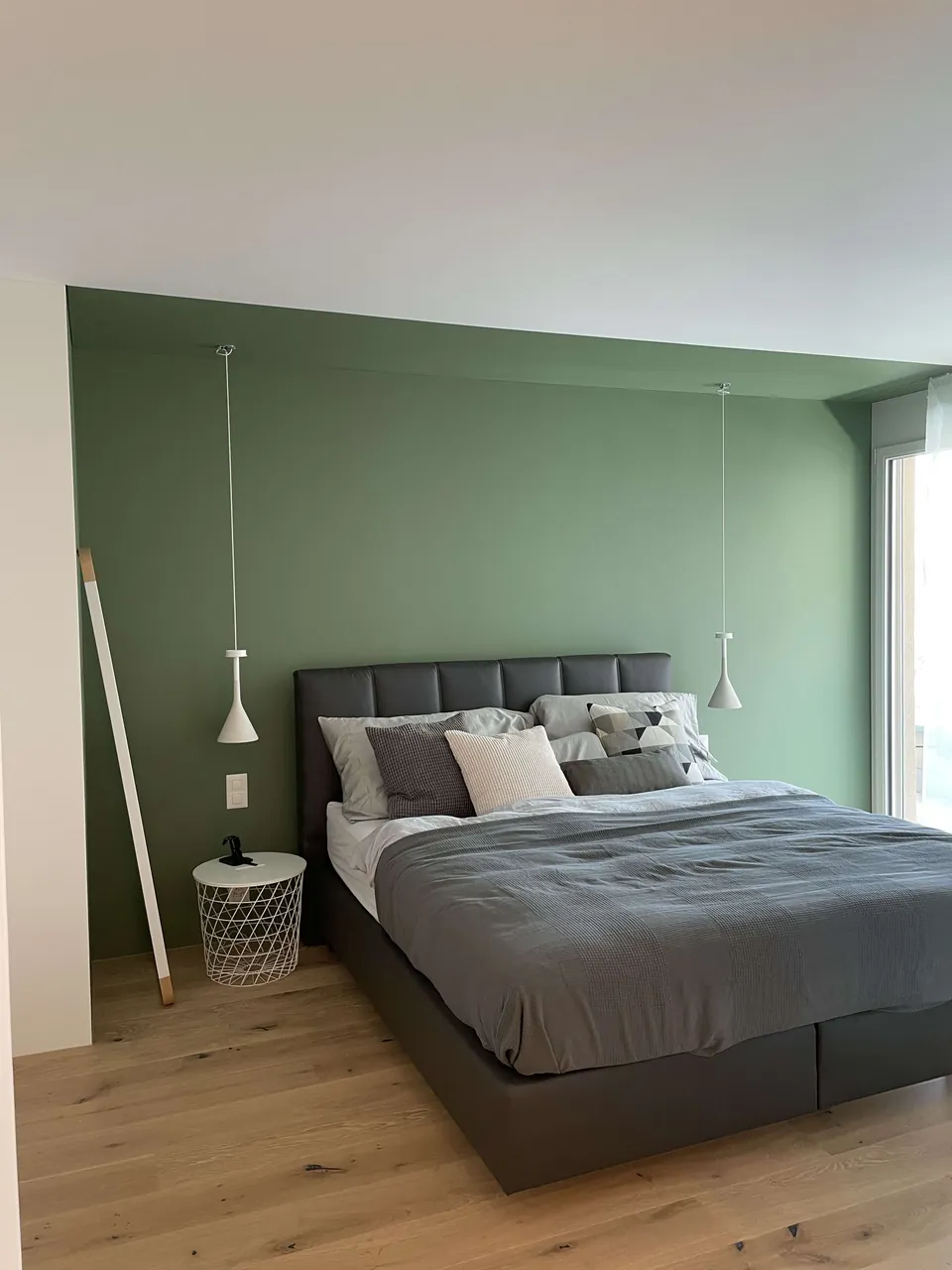 Schlafzimmer mit grün gestrichener Wand hinter dem Bett