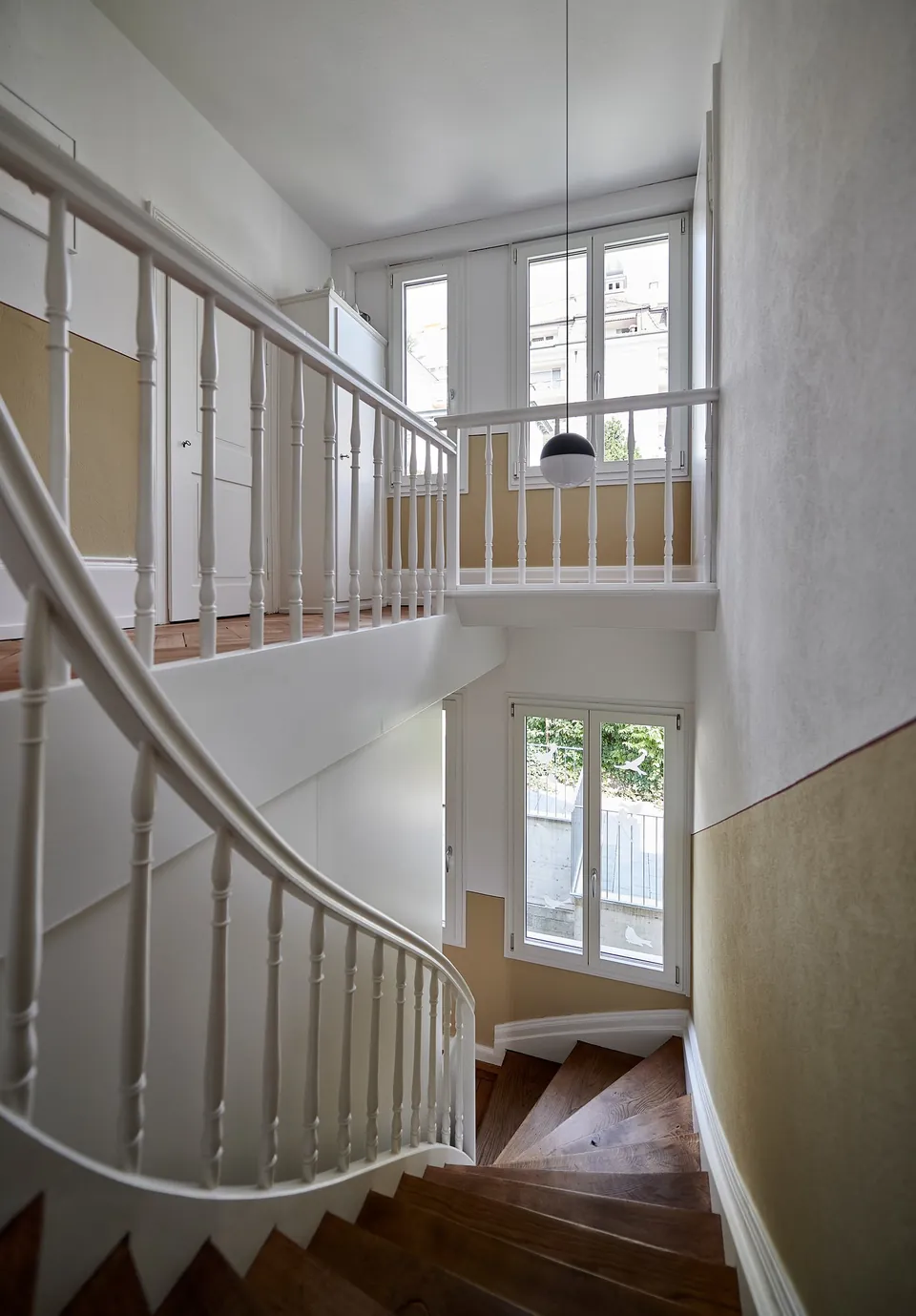 Treppenhaus mit geschwungener Treppe und hellen Wänden im Altbau