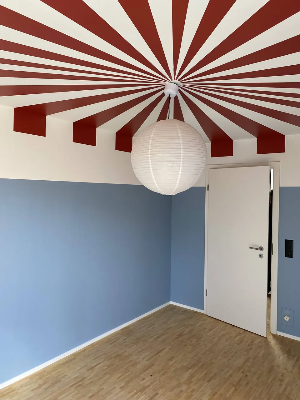 Rot-weiss gestreifte Decke in Strahlenform über hellblauen Wänden