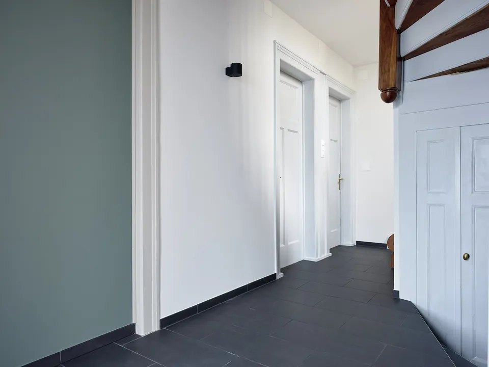 Altbau-Korridor mit graugrüner Wand, weissen Türen und Holztreppe nach dem Farbkonzept mit KT.Color