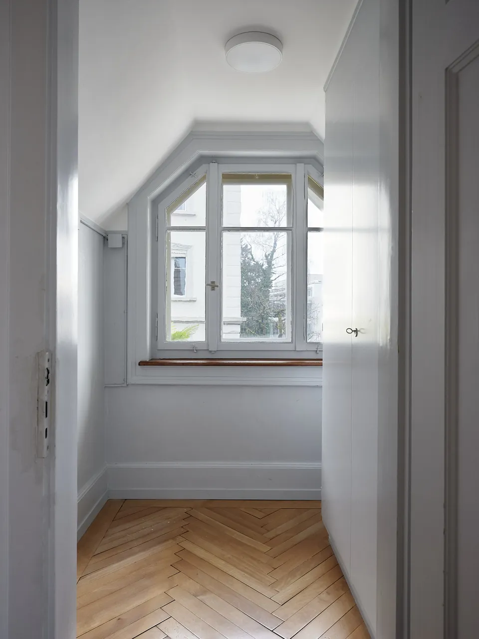 Kleines Zimmer mit Fischgratparkett und Fenster unter der Dachschräge