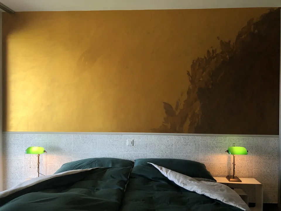 Schlafzimmer mit goldener Wand über einer Tapete mit Schriftbild