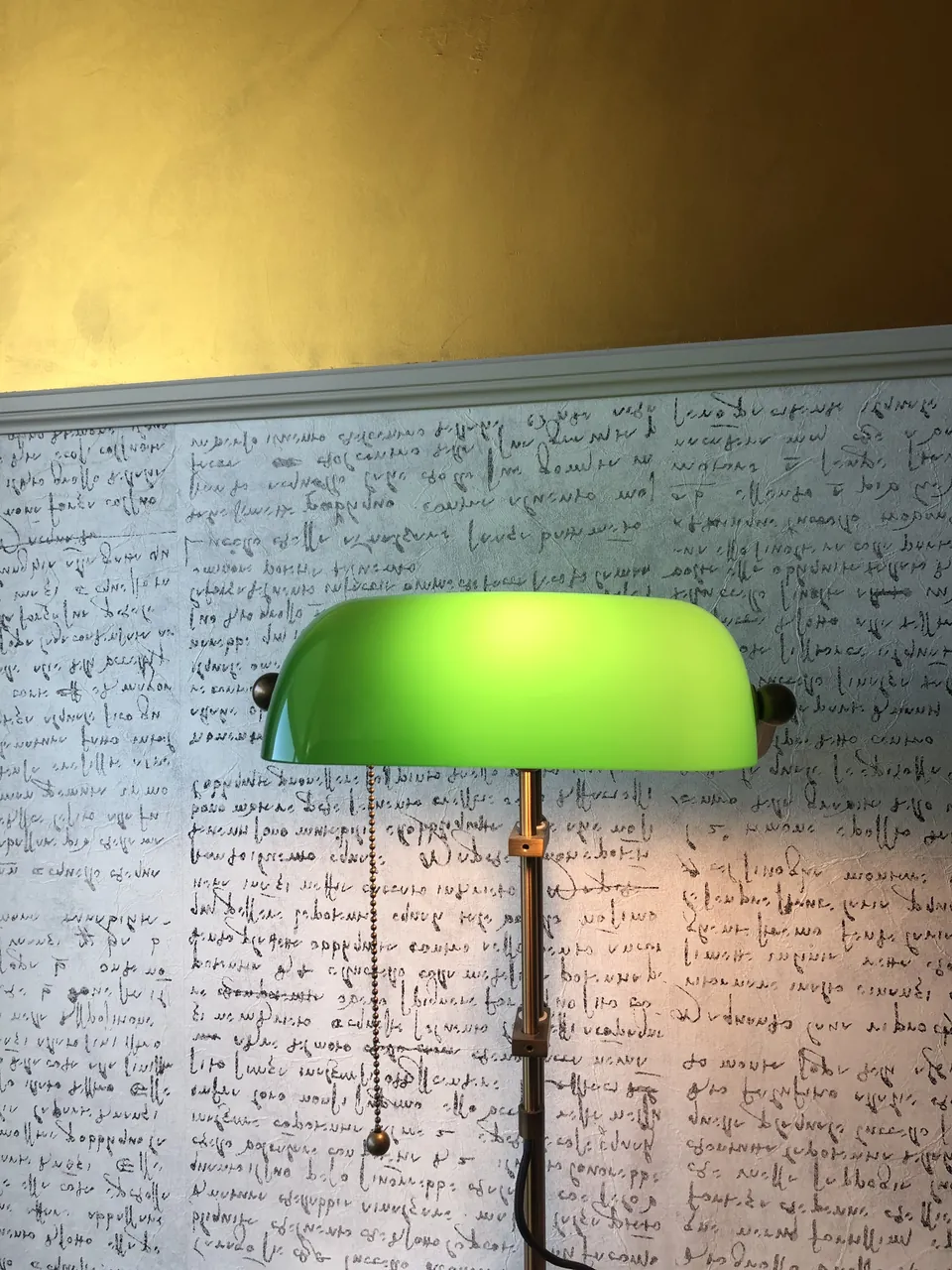 Tapete mit Handschrift, darüber eine Wand in Gold und eine grüne Leselampe