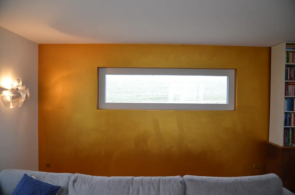 Wohnraum mit Wand in Goldocker und langem, schmalem Fenster über dem Sofa